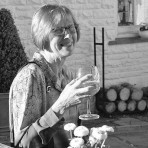 Greyscale photo of Marie, seated in a garden context, holding a glass of drink