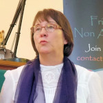 Colour photo of head and shoulders of Maureen, indoors, dressed in a white blouse with a dark purple translucent scarf