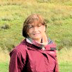 Colour photo of head and shoulders of Rita, in outdoor clothing, with a heathland background